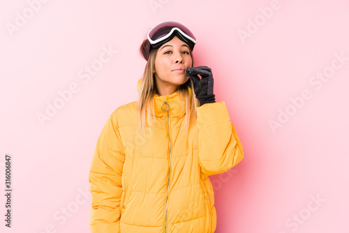 Young caucasian woman wearing a ski clothes in a pink background with fingers on lips keeping a secret.