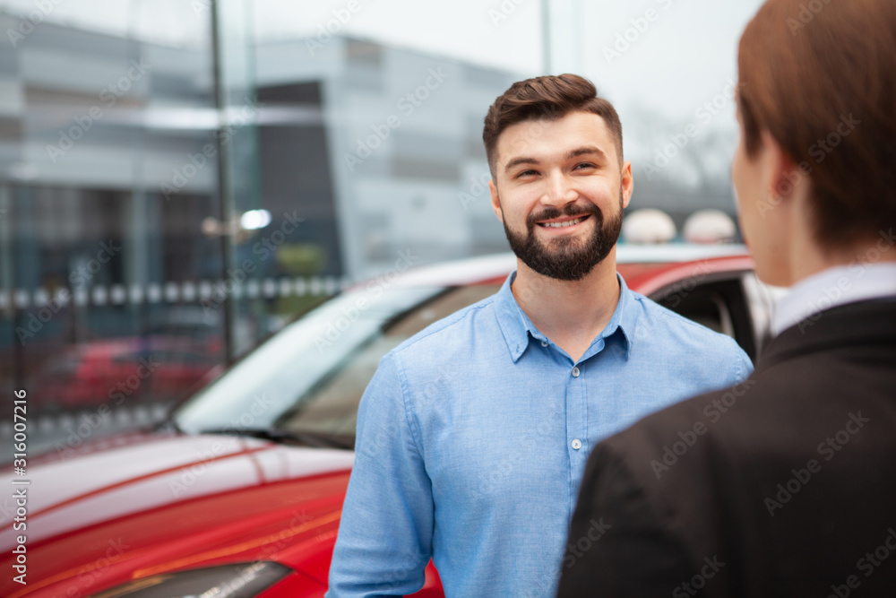 Cheerful handsome man smiling joyfully while talking to car dealership manager, buying new car, copy space Cheerful handsome man smiling joyfully while talking to car dealership manager, buying new car, copy space