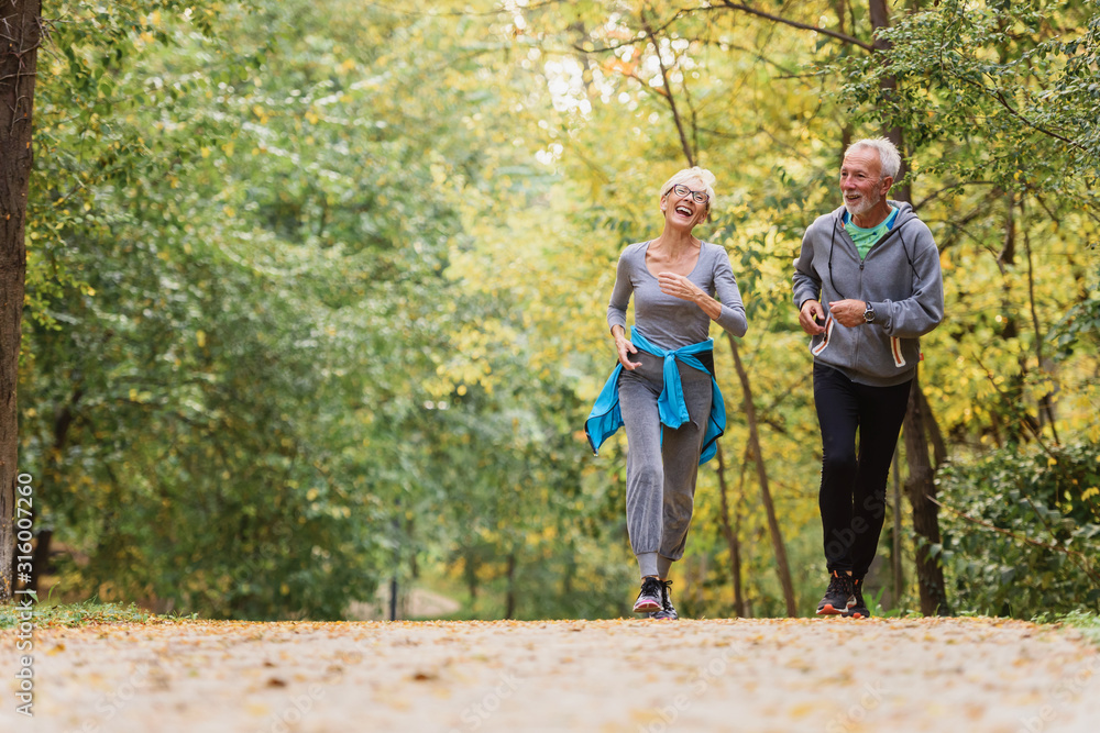 Fototapeta premium Cheerful active senior couple jogging in the park. Exercise together to stop aging.