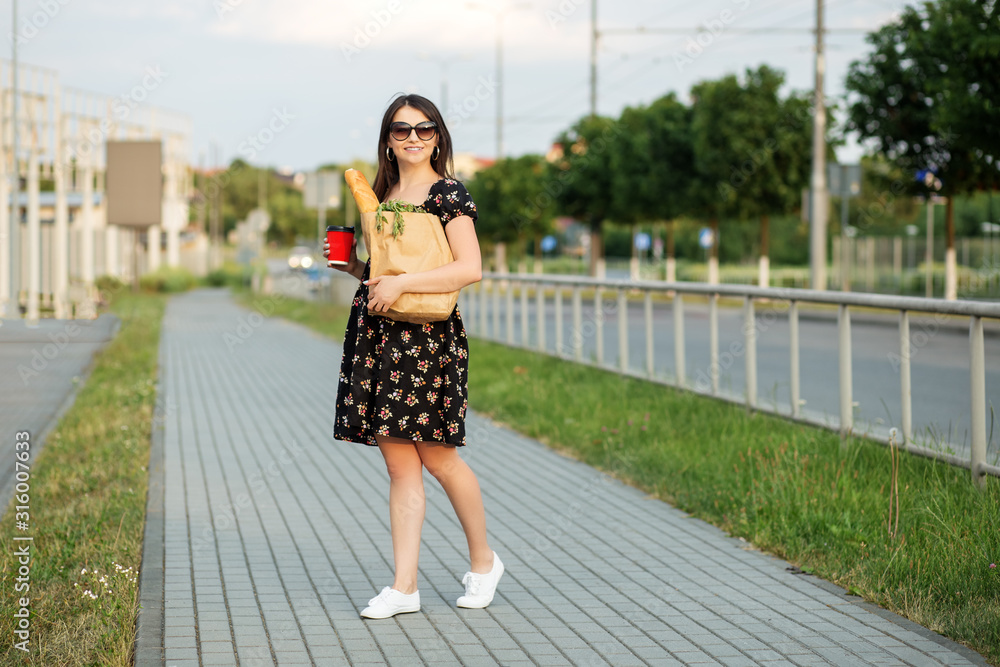 A young woman holds a grocery bag and a glass of coffee. The concept of shopping, eco shopping, lifestyle. A young woman holds a grocery bag and a glass of coffee. The concept of shopping, eco shopping, lifestyle.