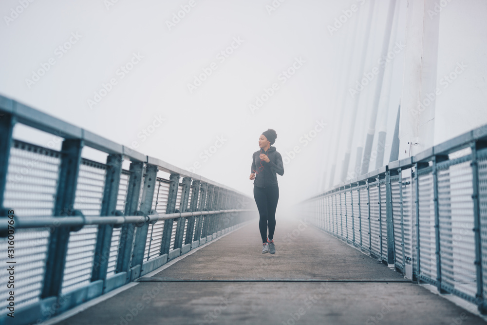A woman jogging on a bridge on a misty day.