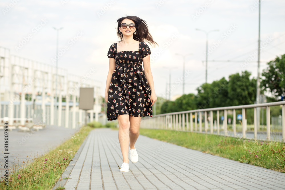 Adult smiling girl is walking down the street in a summer dress. The concept of the style of life, urban and active life.