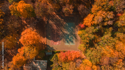 aerial drone view from above on tennis court between trees of a forest, autumn