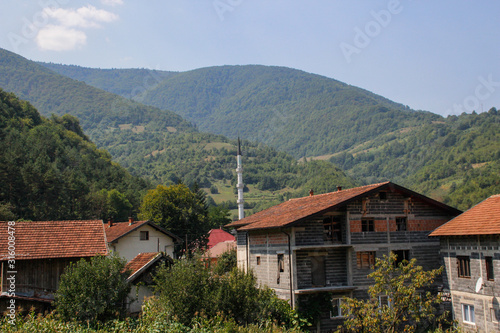 cozy rural houses among the trees and the river with visible minarets of the mosque. Architecture of residential buildings in Bosnia and Herzegovina. © Tanya Hendel
