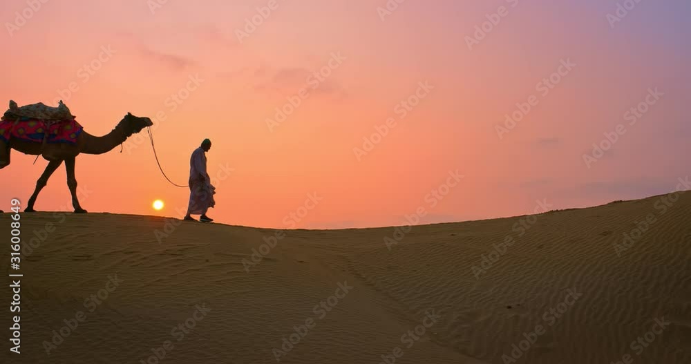 Indian cameleers (camel driver) bedouin with camel silhouettes in sand dunes of Thar desert on sunset. Caravan in Rajasthan travel tourism background safari adventure. Jaisalmer, Rajasthan, India Indian cameleers (camel driver) bedouin with camel silhouettes in sand dunes of Thar desert on sunset. Caravan in Rajasthan travel tourism background safari adventure. Jaisalmer, Rajasthan, India
