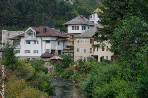 rural houses among the trees and the river with visible minarets of the mosque. Architecture of residential buildings in Bosnia and Herzegovina.
