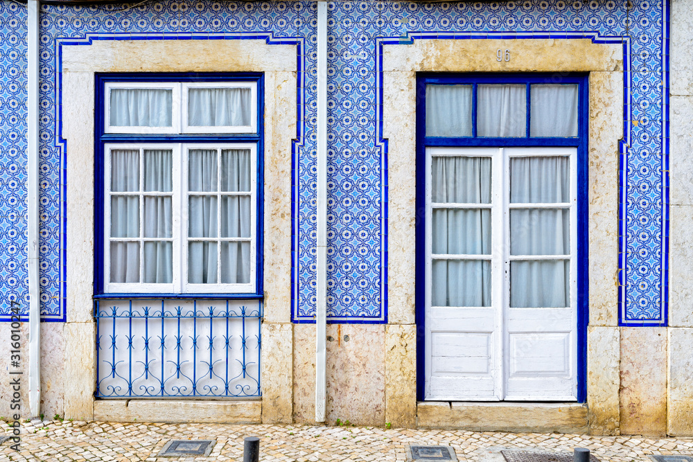 Obraz premium Colorful wooden doors and windows in the facade of a typical Portuguese house - facade covered with azulejos tiles