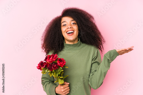 Young afro woman holding a roses isolated Young afro woman holding a rosesreceiving a pleasant surprise, excited and raising hands.