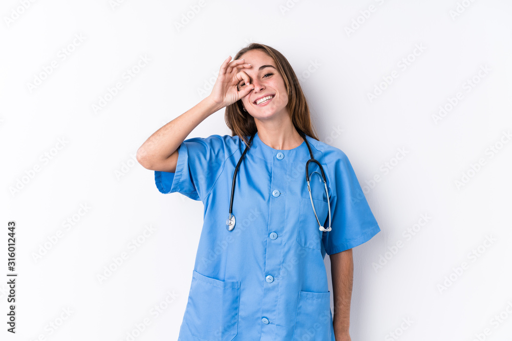 Young nurse woman isolated excited keeping ok gesture on eye. Young nurse woman isolated excited keeping ok gesture on eye.