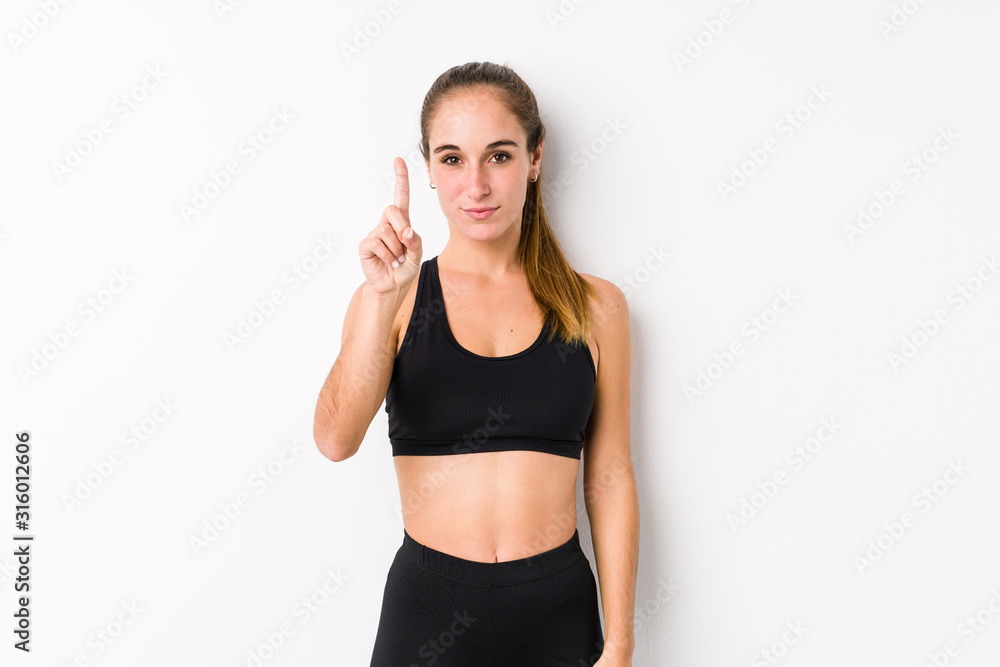 Young caucasian fitness woman posing in a white background showing number one with finger. Young caucasian fitness woman posing in a white background showing number one with finger.