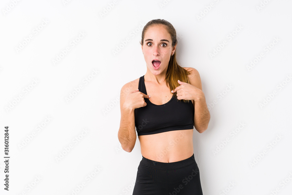 Young caucasian fitness woman posing in a white background surprised pointing with finger, smiling broadly. Young caucasian fitness woman posing in a white background surprised pointing with finger, smiling broadly.