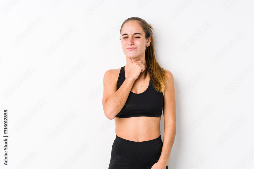 Young caucasian fitness woman posing in a white background suffers pain in throat due a virus or infection. Young caucasian fitness woman posing in a white background suffers pain in throat due a virus or infection.