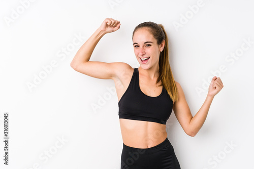 Young caucasian fitness woman posing in a white background celebrating a special day, jumps and raise arms with energy.