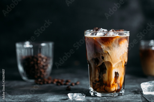 Fototapete Milk Being Poured Into Iced Coffee on a dark table