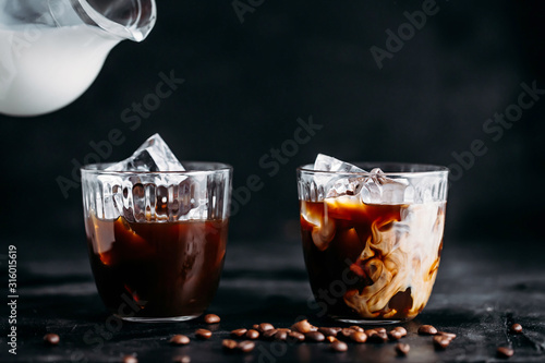 Leinwand Poster Pouring milk into a glass of espresso coffee with ice