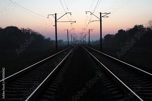 Two tracks of railroad tracks receding towards sunset.