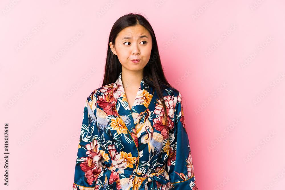 Young chinese woman wearing a kimono pajama isolated confused, feels doubtful and unsure. Young chinese woman wearing a kimono pajama isolated confused, feels doubtful and unsure.