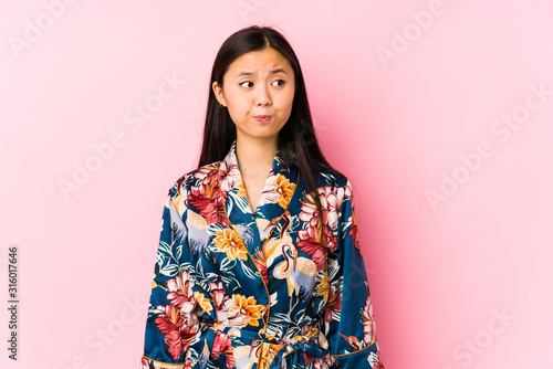 Young chinese woman wearing a kimono pajama isolated confused, feels doubtful and unsure.