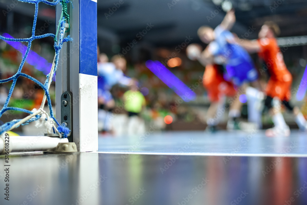 Obraz premium Detail of handball goal post with net and handball match in the background.