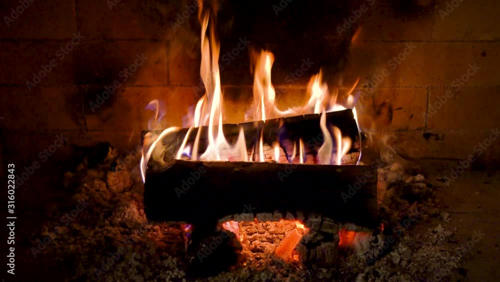 A close-up of wood is burning in the fireplace, with red-hot coals under it