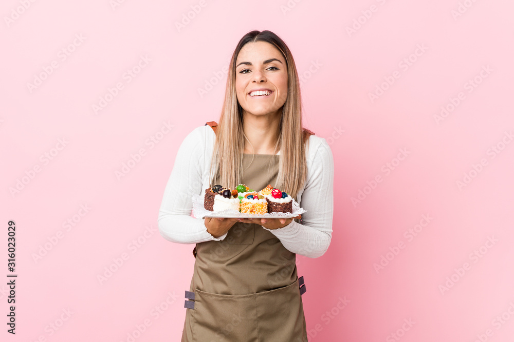 Young baker woman holding sweets laughing and having fun. Young baker woman holding sweets laughing and having fun.