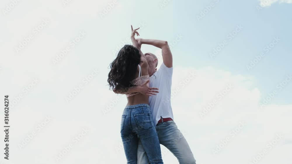 People are wearing jeans. They are close to each other. A man and woman are outdoors. People are wearing jeans. They are close to each other. A man and woman are outdoors.