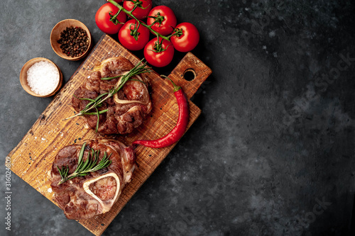 two steaks on the grill, with tomatoes and spices on a stone background, with copy space for your text. dinner concept for two