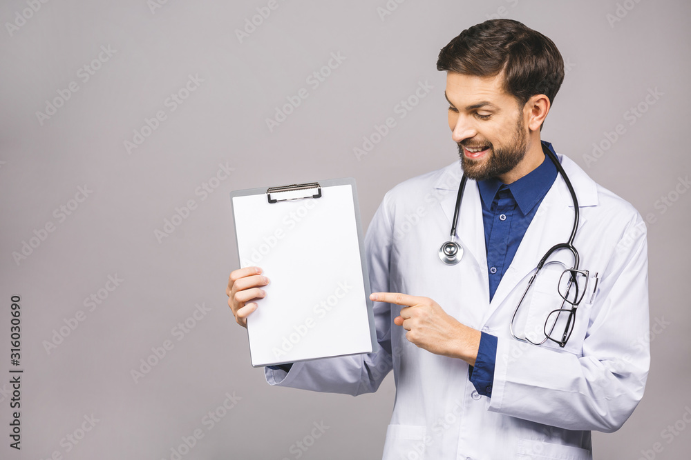 Portrait of bearded smiling intern, who is holding the clipboard with empty paper. Doctor is wearing white uniform, stands over isolated grey background, showing blank. Portrait of bearded smiling intern, who is holding the clipboard with empty paper. Doctor is wearing white uniform, stands over isolated grey background, showing blank.
