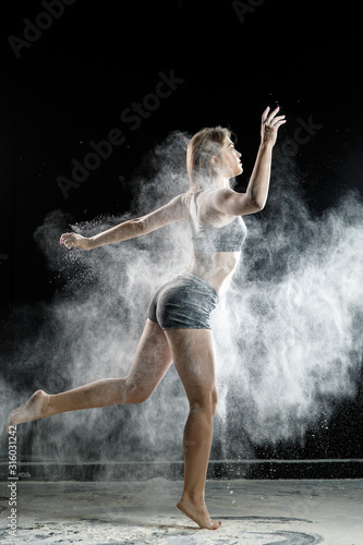 Beautiful girl model on a black background throws flour