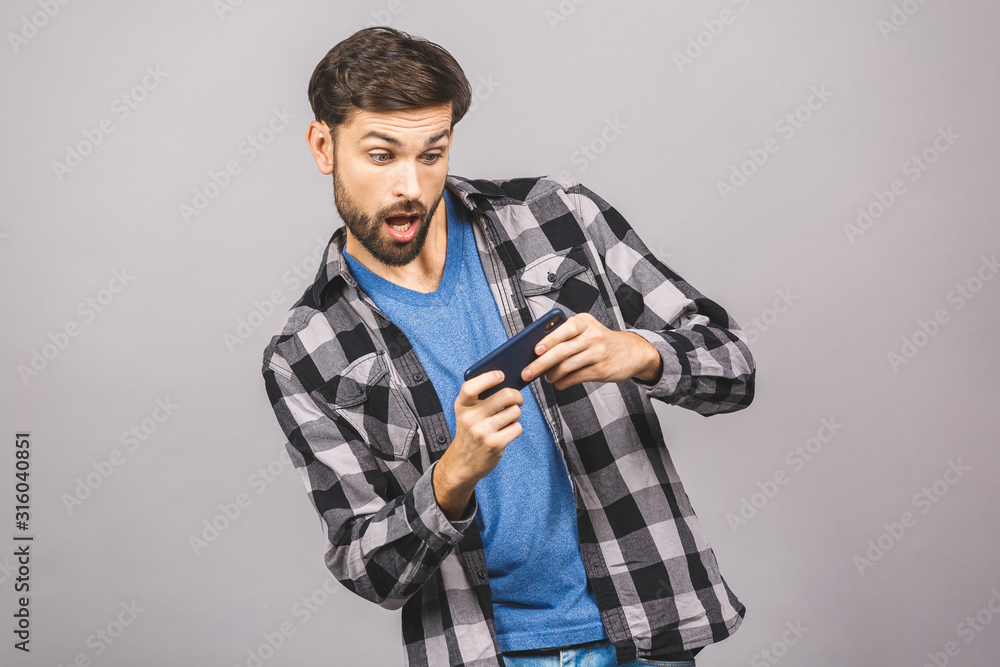 Portrait of an excited young man in casual playing games on mobile phone isolated over grey background. Portrait of an excited young man in casual playing games on mobile phone isolated over grey background.