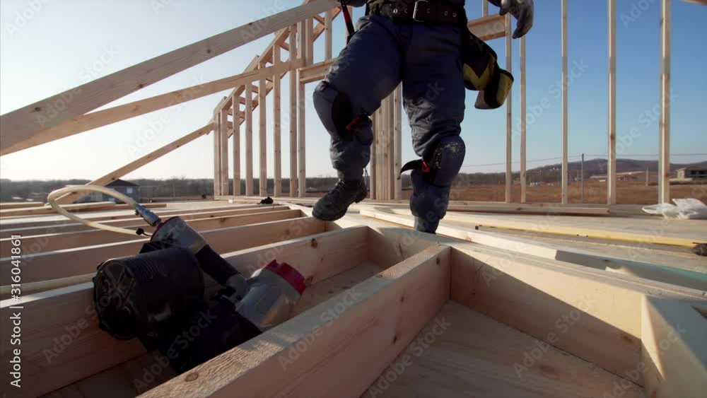 Builder is adjusting wooden planks with manual and hydraulic hammer at frame house building at sunny day