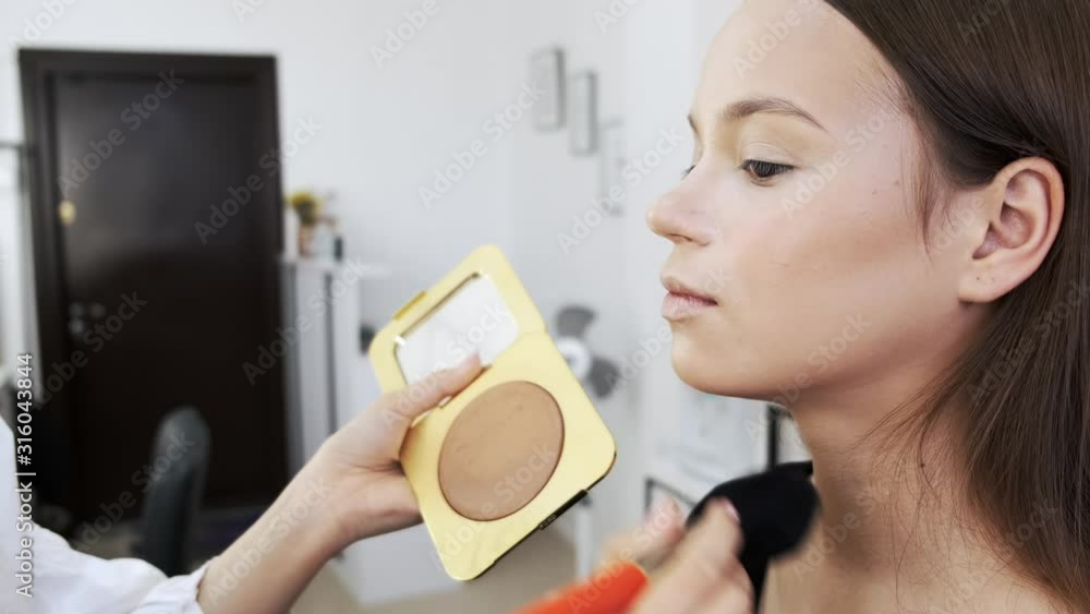 An artist uses powder. She is doing a makeup. A client is in the salon. An artist uses powder. She is doing a makeup. A client is in the salon.
