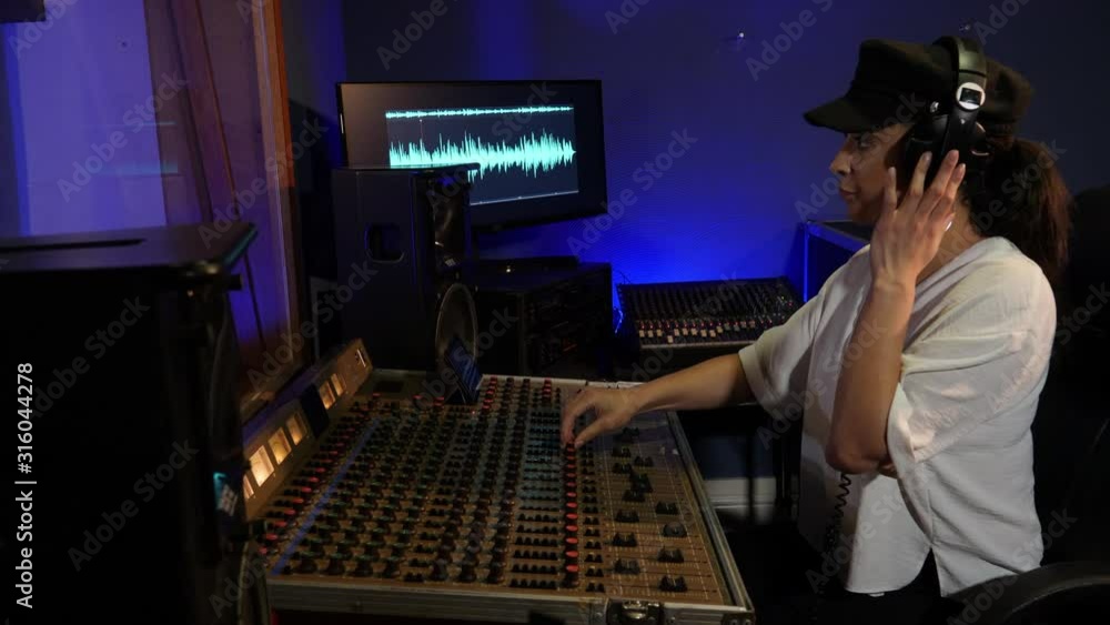 4K: Female Sound Engineer mixing a track in a recording Studio. she is at the Desk with Headphones on 4K: Female Sound Engineer mixing a track in a recording Studio. she is at the Desk with Headphones on