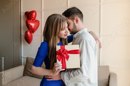 man and woman with present in gift box with red heart shaped balloons at home