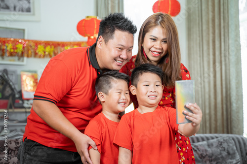 Asian family with two son smiling holding cell phone to take selfie with father and mother.Asian Chinese family celebrates Lunar New Year