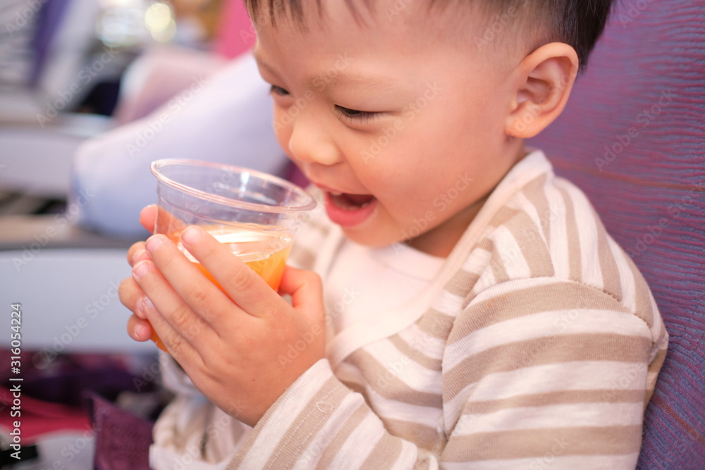 Cute little Asian 2 - 3 years old toddler baby boy child drinking orange juice during flight on airplane. Flying with children, Happy air travel with kids & little traveler concept, Selective focus Cute little Asian 2 - 3 years old toddler baby boy child drinking orange juice during flight on airplane. Flying with children, Happy air travel with kids & little traveler concept, Selective focus