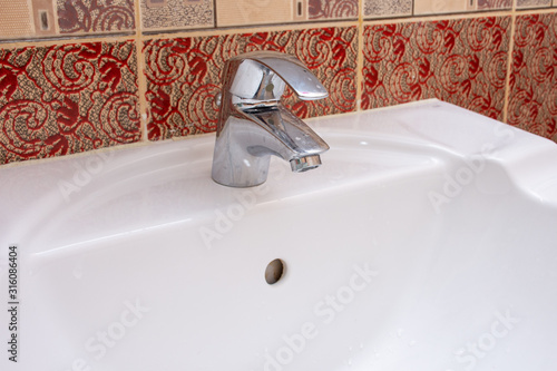 Shiny residential silver bathroom faucet or tap on a white ceramic sink. Plumbing, DIY, or maintenance concepts. photo