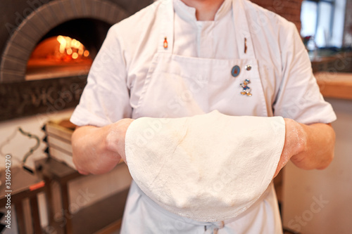 Dough for Neapolitan pizza, the chef rolls out the blanks. Closeup hand of chef baker in uniform white apron cook pizza at kitchen photo