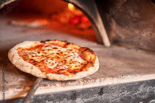 Baked tasty margherita pizza in Traditional wood oven in Naples restaurant, Italy. Original neapolitan pizza. Red hot coal.