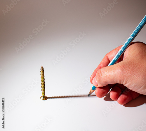 A screw with it's shadow, with a hand holding a pencil at the end. Shadow of screw drawn by a hand, with a pencil. photo