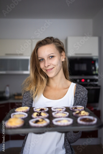 Pretty, young woman baking gluten free cupkes - taking them out of the oven, being pleased with the result photo