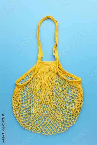 Zero waste concept. A reusable mesh yellow shopping bag lies on blue background. Vertical orientation, top view.