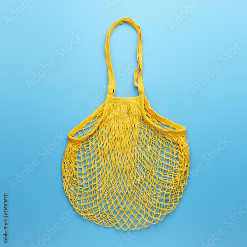 Zero waste concept. Reusable mesh yellow shopping bag for food products lies on blue background.