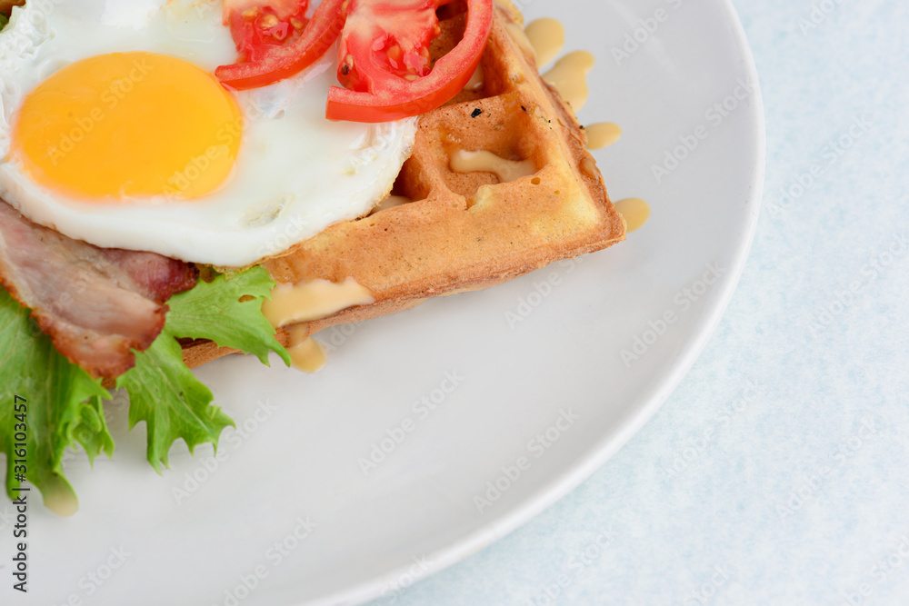 Classic eggs and bacon on waffles breakfast with tomatoes and salad served on a white plate on white background. Classic eggs and bacon on waffles breakfast with tomatoes and salad served on a white plate on white background.