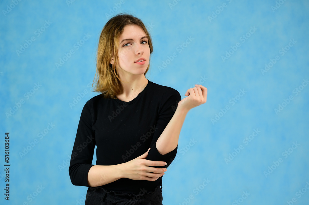 Studio portrait of a pretty blonde girl in a black T-shirt on a blue background with bright emotions. A universal concept, the picture is suitable for any topic. Studio portrait of a pretty blonde girl in a black T-shirt on a blue background with bright emotions. A universal concept, the picture is suitable for any topic.