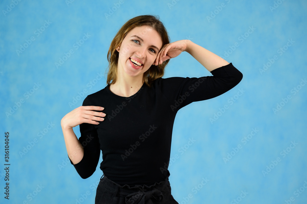 Fototapeta premium Studio portrait of a pretty blonde girl in a black T-shirt on a blue background with bright emotions. A universal concept, the picture is suitable for any topic.