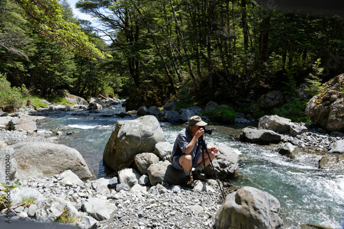 A photographer is crouched down behind his tripod taking photos of a river