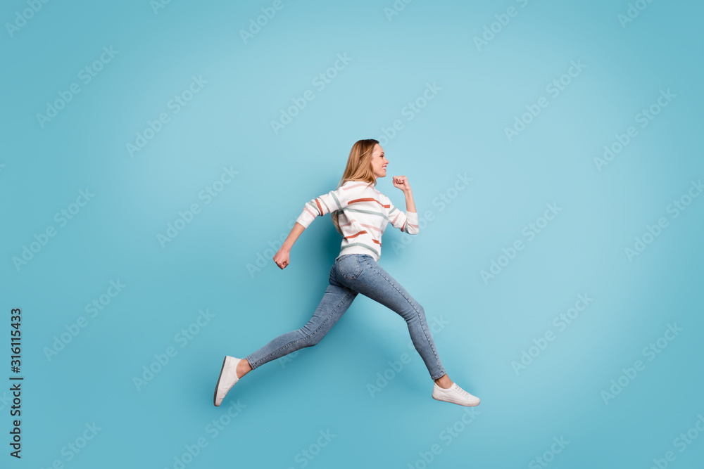 Side profile full length body size photo of cheerful positive pretty sweet girlfriend smiling toothily in jeans denim running jumping isolated pastel blue color background
