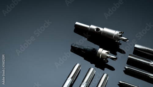 Closeup straight flute tap tip and hole saw on dark background. Industrial tapping tools. Carbide tip metal cutter. Metalworking hardware. Mechanic tools. Drilling equipment. Mechanical engineering.