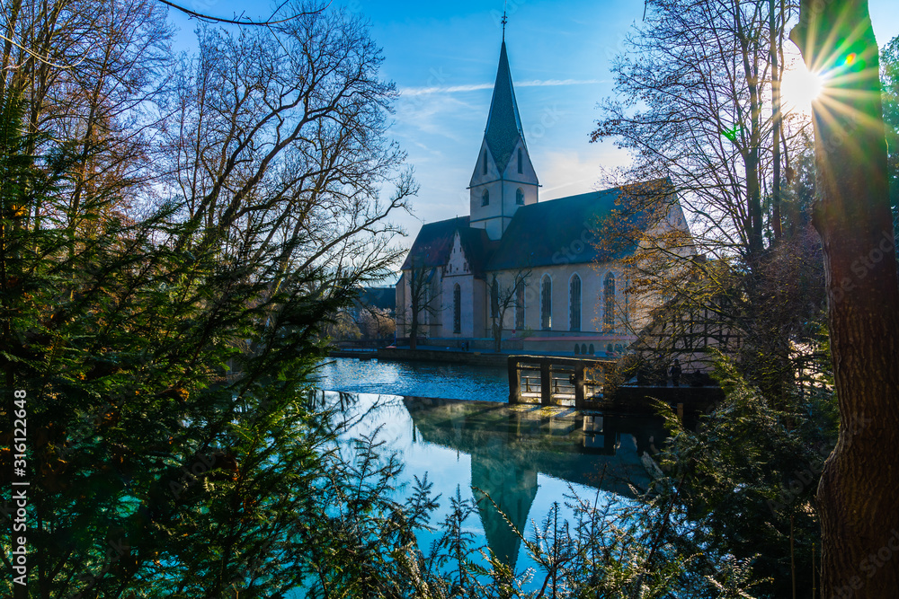 Germany, Early morning fog moving over blue water surface of blue pot or german blautopf in blaubeuren forest reflecting beautiful church building in calm water